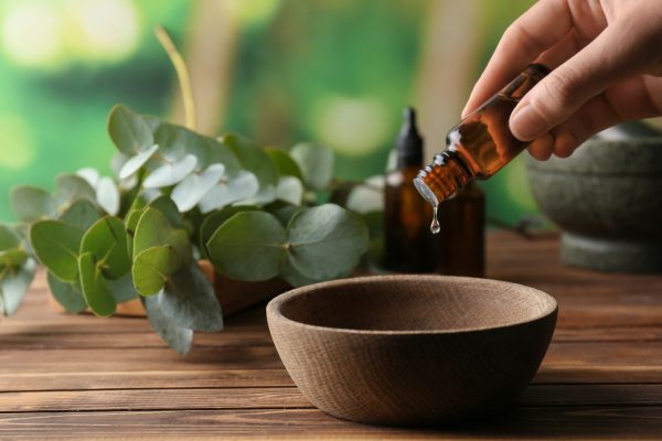 Woman pouring eucalyptus essential oil into bowl on wooden table