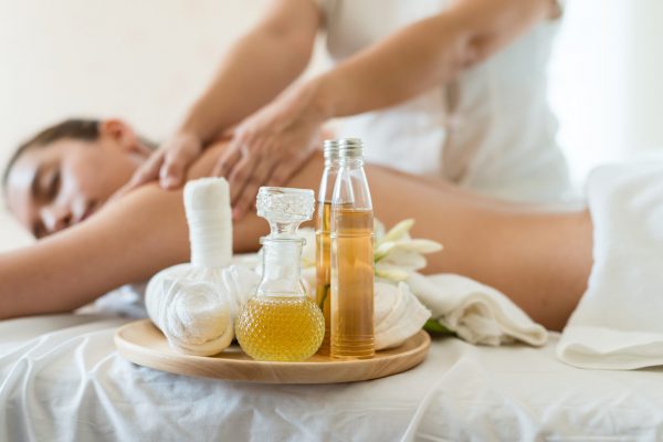 Bottle of essential oil on a wooden tray. background Young beautiful Asian woman relaxing in the spa massage